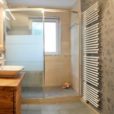 Der Duschbereich ist durch eine Glaswand abgetrennt, während eine große Fensteröffnung für Tageslicht sorgt.