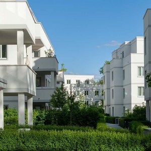 Helle Architektur umgeben von üppigem Grün und Bäumen Architektonisch ansprechende Wohnhäuser, die in einer ruhigen Umgebung mit gepflegten Hecken und Bäumen stehen.