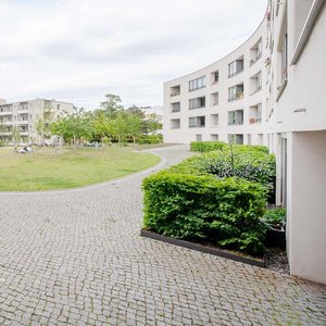 Der Innenhof einer Wohnanlage, umgeben von hellen Gebäuden, bietet eine grüne Rasenfläche und gemütliche Sitzgelegenheiten.