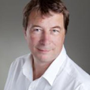 Der Mann lächelt leicht, während er in die Kamera schaut, mit einem professionellen und einladenden Auftreten.