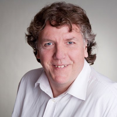 Der Mann hat eine entspannte Ausstrahlung, mit einem breiten Lächeln und einem hellen Hintergrund.