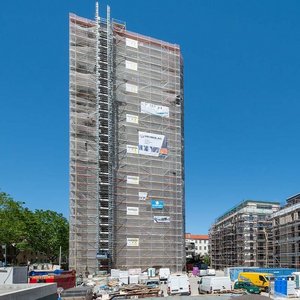 Eine Baustelle mit einem hohen, gerüsteten Gebäude und einem niedrigeren, ebenfalls eingerüsteten Gebäude im Vordergrund.
