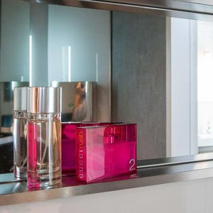 Ein eleganter Spiegel reflektiert zwei Parfümflaschen, eine in klarem Glas und die andere in leuchtendem Pink.