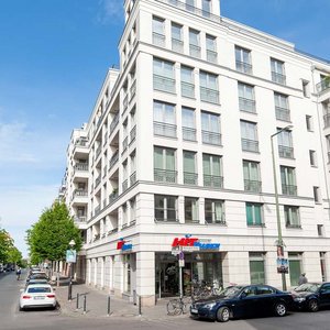 Helle Wohngebäude umgeben von grünen Bäumen Die Ecke eines modernen Wohngebäudes mit großen Fenstern, das von einer ruhigen Stadtstraße umgeben ist.