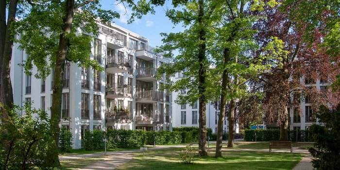 Ein ruhiger Park mit gepflegten Rasenflächen, Bänken und hohen Bäumen, die Schatten spenden und eine entspannte Atmosphäre schaffen.