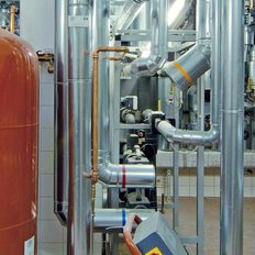Die Anlage zeigt eine Vielzahl von glänzenden Metallrohren und Ventilen, die in einem technischen Raum angeordnet sind.