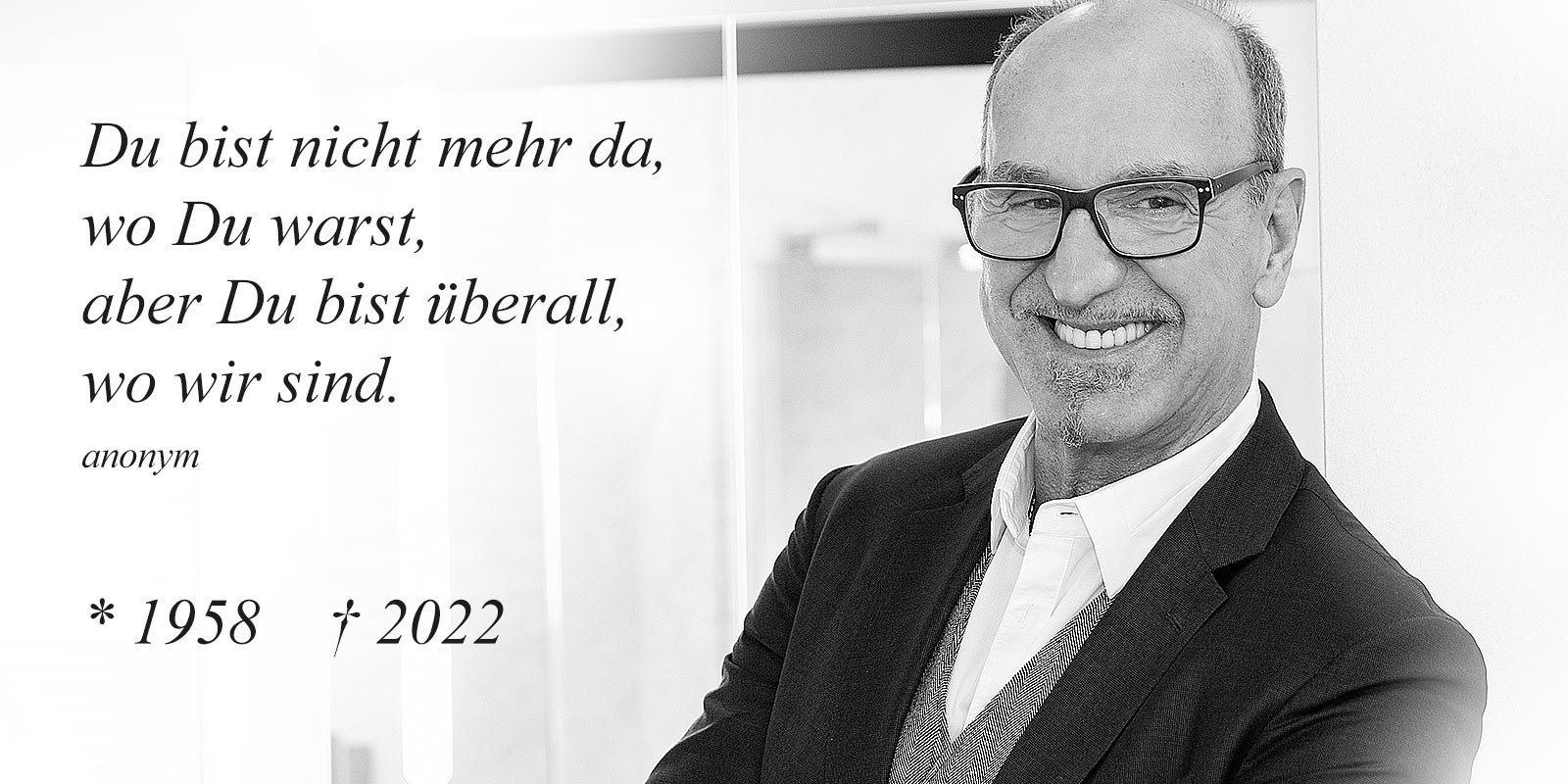 Ein lächelnder Mann in einem Anzug steht vor einer hellen Wand, während er eine nachdenkliche Botschaft teilt.