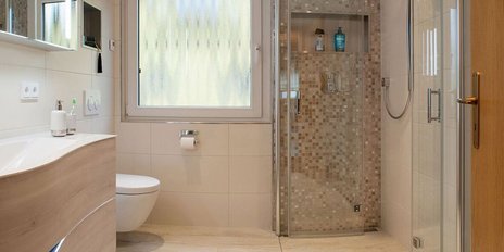 Helles Badezimmer mit großen Fenstern, das eine Dusche, ein WC und einen stilvollen Waschtisch zeigt.