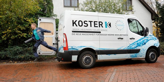 Ein Techniker springt aus einem Lieferwagen, bereit für einen Einsatz in einem Wohngebiet mit herbstlichen Bäumen im Hintergrund.