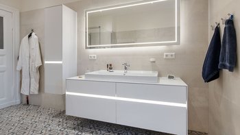 Ein modernes Badezimmer mit einem eleganten Waschbecken und einem großen, beleuchteten Spiegel über dem Waschbecken.