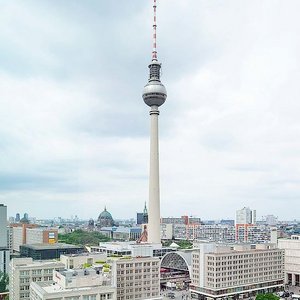 Belebter Platz mit dem Fernsehturm im Hintergrund Ein Blick auf den Berliner Fernsehturm, der über die Stadt ragt, während Wolken den Himmel bedecken und Menschen auf dem Platz flanieren.