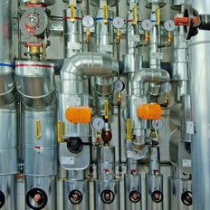 Die Bildkomposition zeigt glänzende Metallrohre, die miteinander verbunden sind, mit verschiedenen Ventilen und Messinstrumenten.