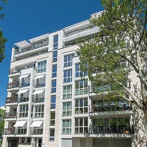 Helle Architektur eines Mehrfamilienhauses im Stadtzentrum Die Fassade eines eleganten Mehrfamilienhauses, das von einer ruhigen Straße mit parkenden Autos flankiert wird.