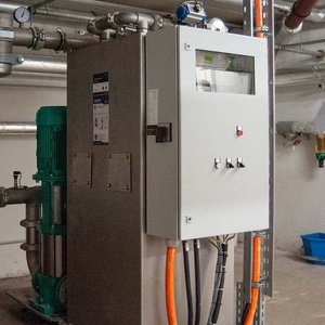 Effiziente Rohrleitungen und Pumpen für Wasserversorgung Im Hintergrund sind metallische Rohre und eine grüne Pumpe zu sehen, die in einem industriellen Umfeld installiert sind.