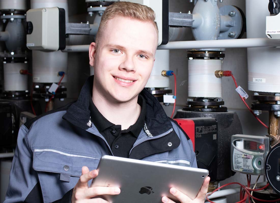 Ein junger Anlagenmechaniker vor einer Heizungsanlage, der ein Tablet hält
